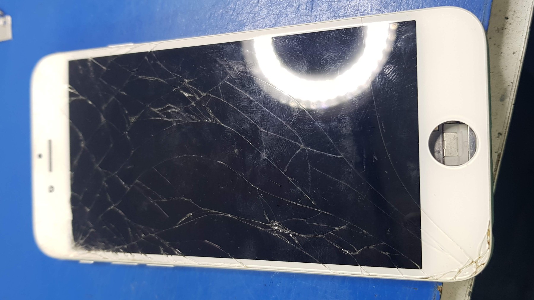 Napuklo staklo telefona na plavoj radnoj podlozi
