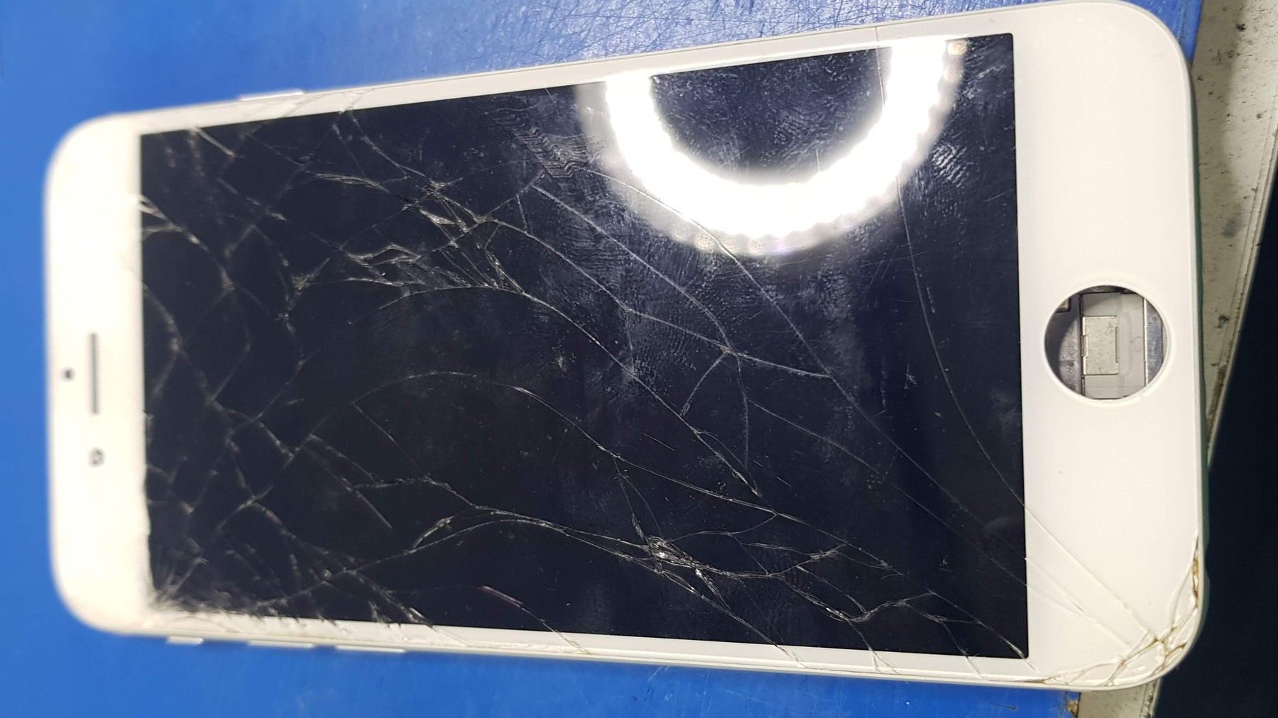 Napuklo staklo telefona na plavoj radnoj podlozi